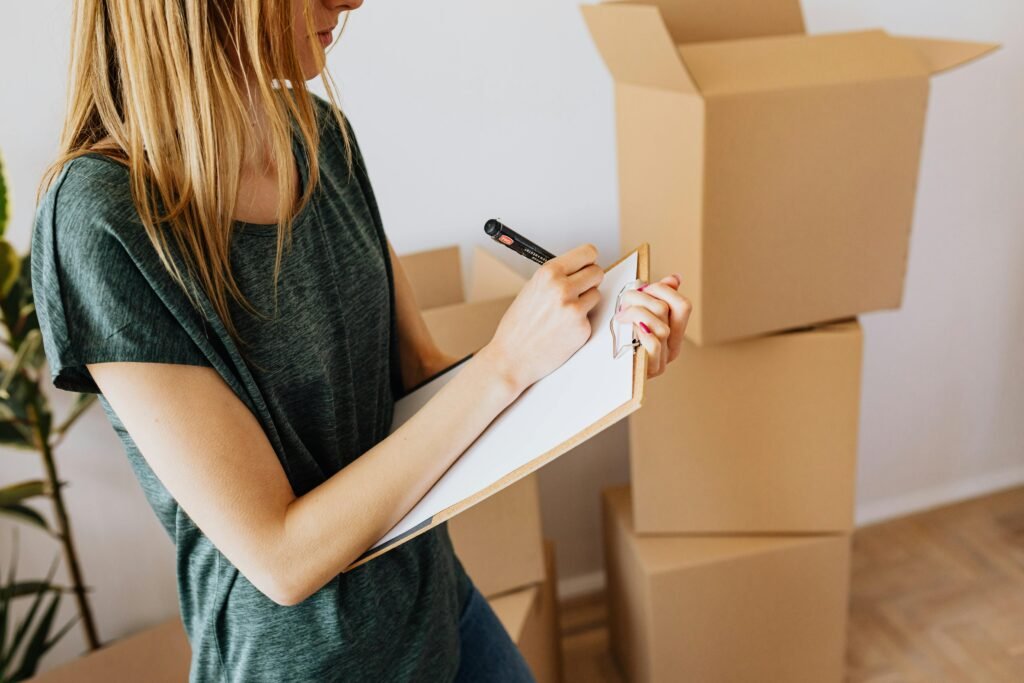 pexels-photo-4506243-4506243 A young woman writes on a clipboard while organizing moving boxes in her home.
